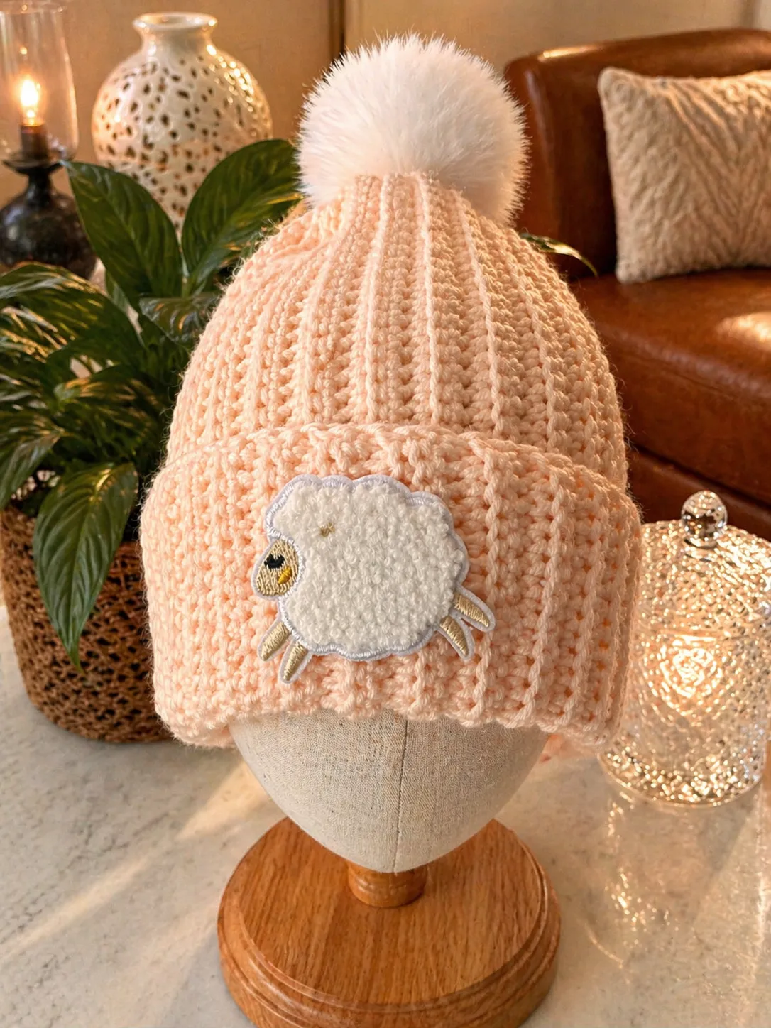 Blush pink hand-crocheted baby beanie with white fluffy pom-pom and cream applique lamb face with embroidered features