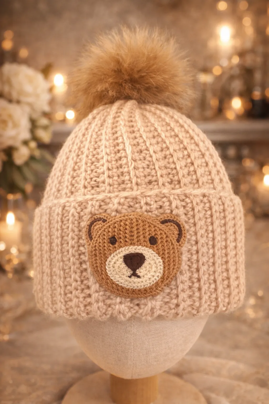 An oatmeal ribbed baby beanie with a small tan bear face on the cuff.