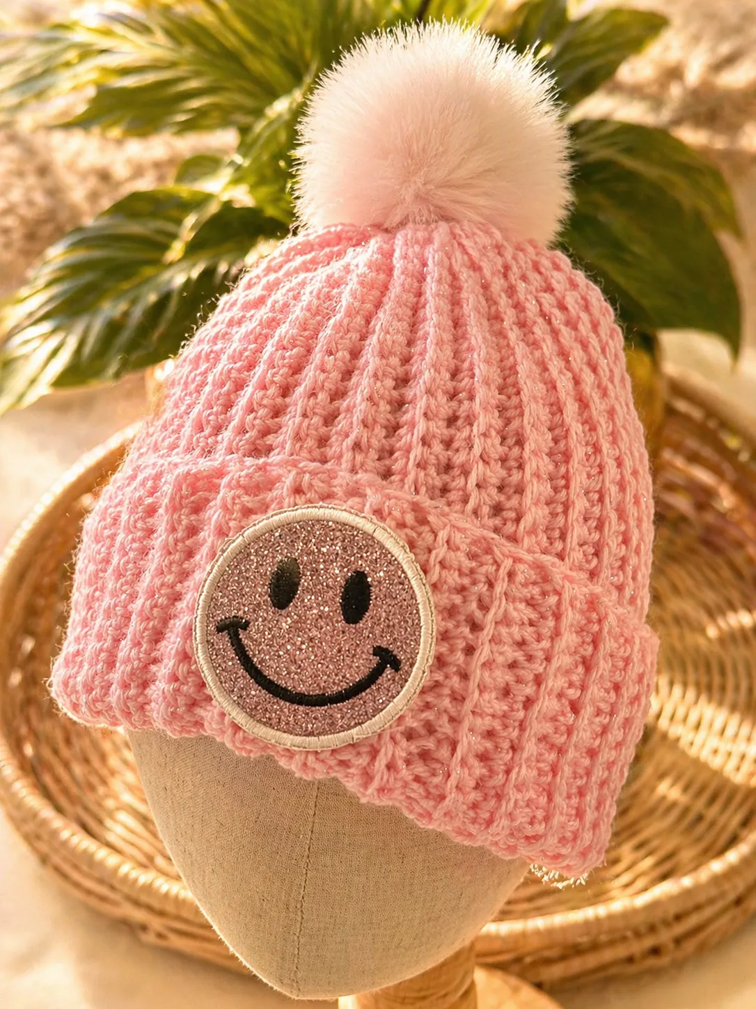 Pink glitter crocheted beanie with pink pom-pom and embroidered glittery smiley face patch&nbsp;