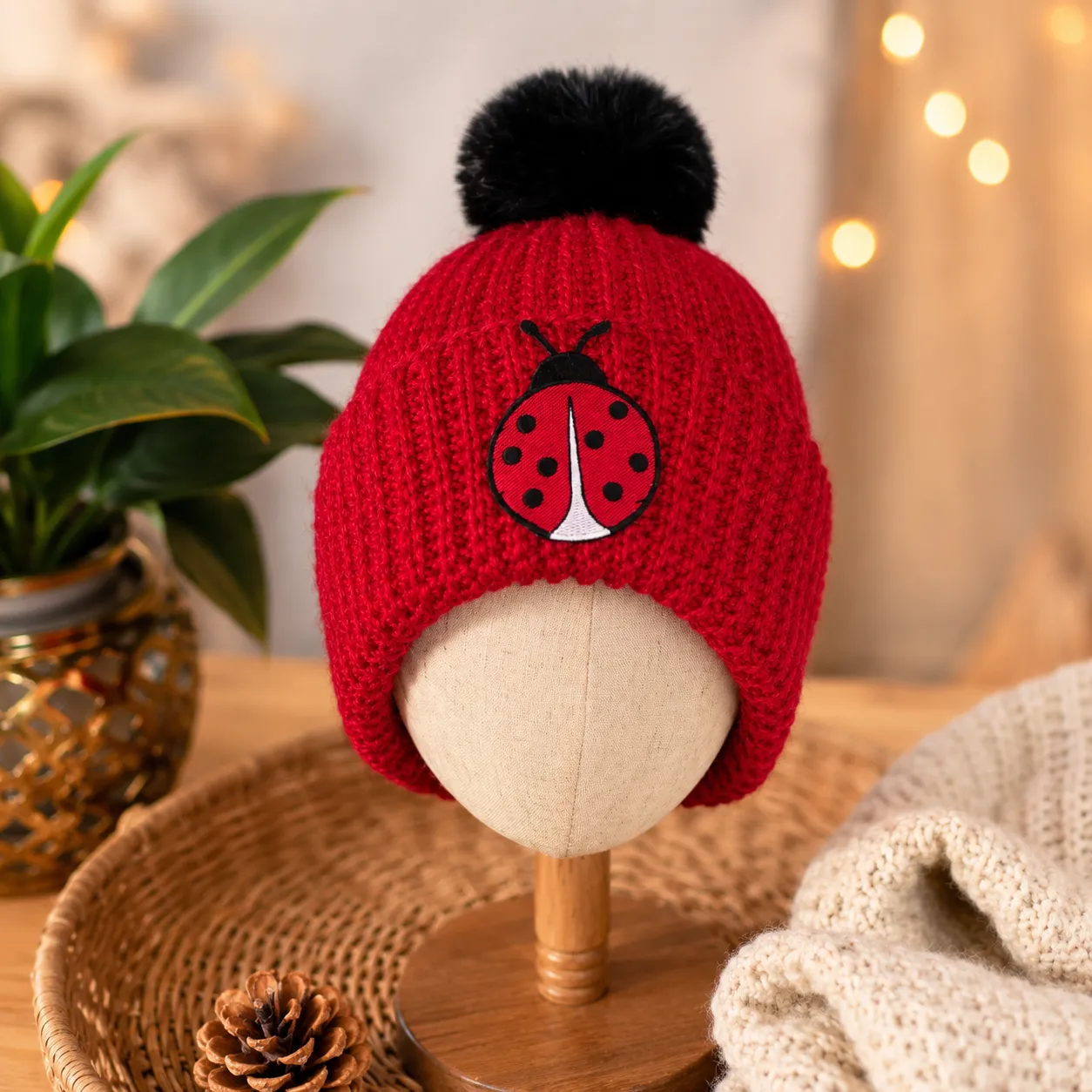 Red crocheted beanie with black pom pom featuring black embroidered ladybug
