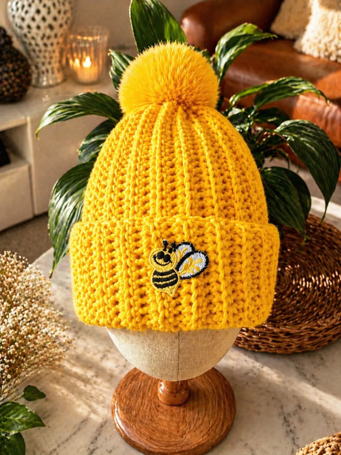 Bright yellow hand-crocheted beanie with ribbed texture, small black and blue bee embroidery, and a fluffy yellow pom pom